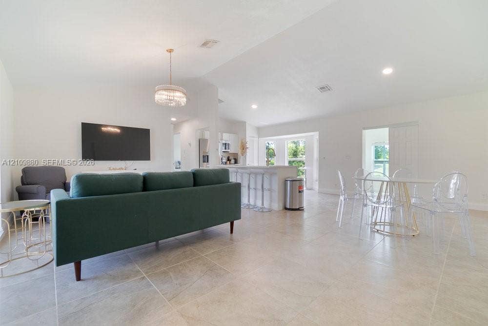 8231 Coconut Boulevard, West Palm Beach, West Palm Beach, FL 33412 Open-concept interior featuring vaulted ceilings, oversized tile flooring, a tiered kitchen island with bar seating, and a decorative tiered chandelier