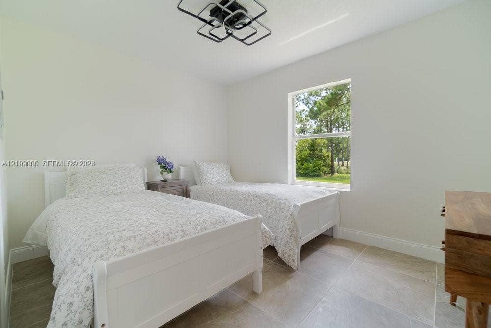 8231 Coconut Boulevard, West Palm Beach, West Palm Beach, FL 33412 Neutral-toned room featuring large-format tile flooring, a geometric flush-mount ceiling light fixture, and a single-hung window with exterior tree-line scenery