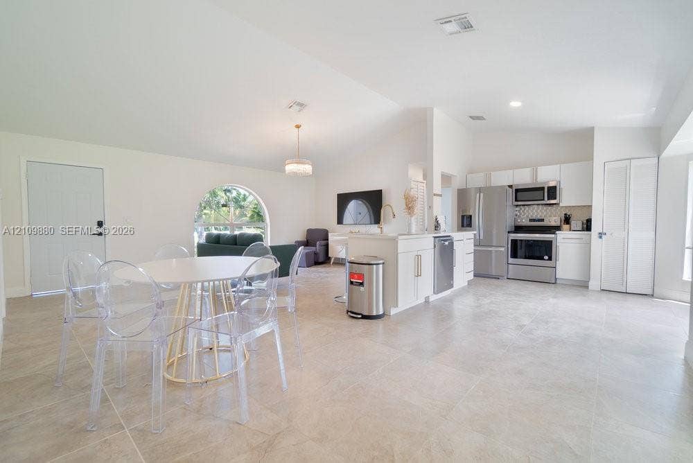 8231 Coconut Boulevard, West Palm Beach, West Palm Beach, FL 33412 Open floor plan featuring vaulted ceilings, neutral large-format tile flooring, a kitchen island with white cabinetry, stainless steel appliances, and an arched window