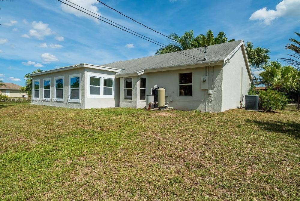 8231 Coconut Boulevard, West Palm Beach, West Palm Beach, FL 33412 Rear exterior featuring a neutral-toned stucco facade, multi-pane windows, a gabled roofline, and an expansive lawn