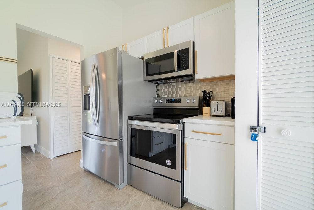 8231 Coconut Boulevard, West Palm Beach, West Palm Beach, FL 33412 Kitchen featuring white shaker-style cabinetry, stainless steel appliances, brushed gold-tone hardware, a tiled backsplash, and stone-finish countertops