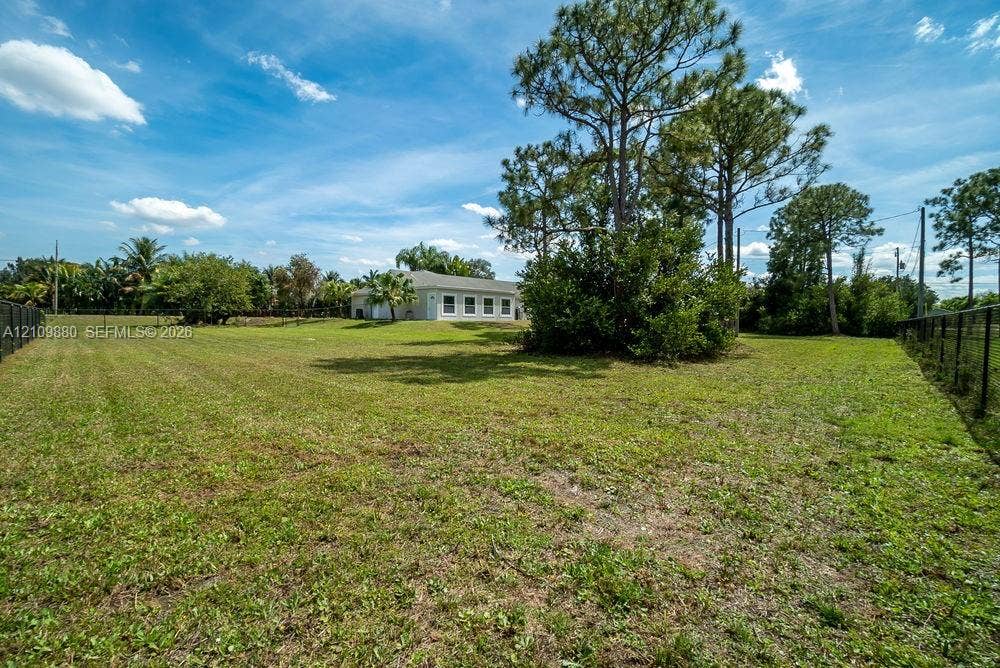 8231 Coconut Boulevard, West Palm Beach, West Palm Beach, FL 33412 Expansive backyard featuring a large grass lawn, mature pine trees, perimeter fencing, and exterior landscape foliage