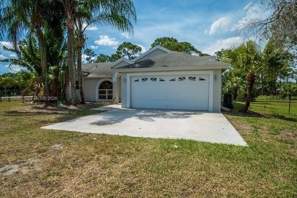8231 Coconut Boulevard, West Palm Beach, West Palm Beach, FL 33412 Single-story exterior featuring a concrete driveway, two-car garage with arched decorative windows, and stucco siding