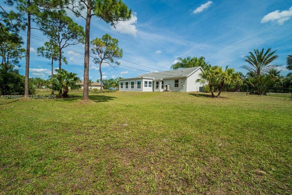 8231 Coconut Boulevard, West Palm Beach, West Palm Beach, FL 33412 Expansive backyard featuring a sprawling lawn, mature pine trees, palm landscaping, and an exterior with an enclosed porch area