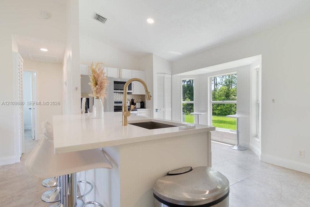 8231 Coconut Boulevard, West Palm Beach, West Palm Beach, FL 33412 Kitchen featuring a central island with a quartz countertop, an undermount sink with a gold-finish gooseneck faucet, tile flooring, and a bay window