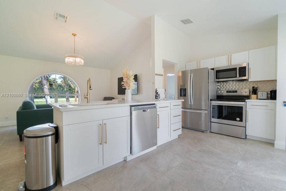 8231 Coconut Boulevard, West Palm Beach, West Palm Beach, FL 33412 Kitchen featuring white shaker cabinetry, stainless steel appliances, large-format tile flooring, a breakfast bar, and a vaulted ceiling with a circular window