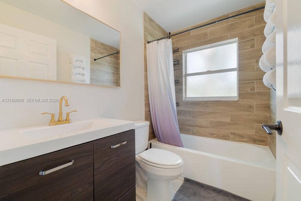 8231 Coconut Boulevard, West Palm Beach, West Palm Beach, FL 33412 Bathroom featuring a vanity with wood-finish cabinetry, a white integrated countertop, brass-tone faucet, large wall-mounted mirror, and a tub-shower combination with wood-finish tile surround
