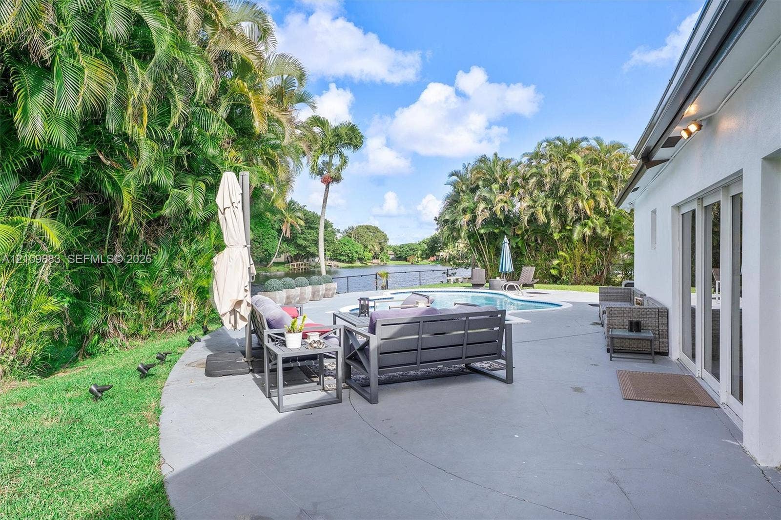 751 SW 54th Avenue, Margate, FL 33068 Outdoor living area featuring a paved patio, swimming pool, water frontage, and mature palm landscaping