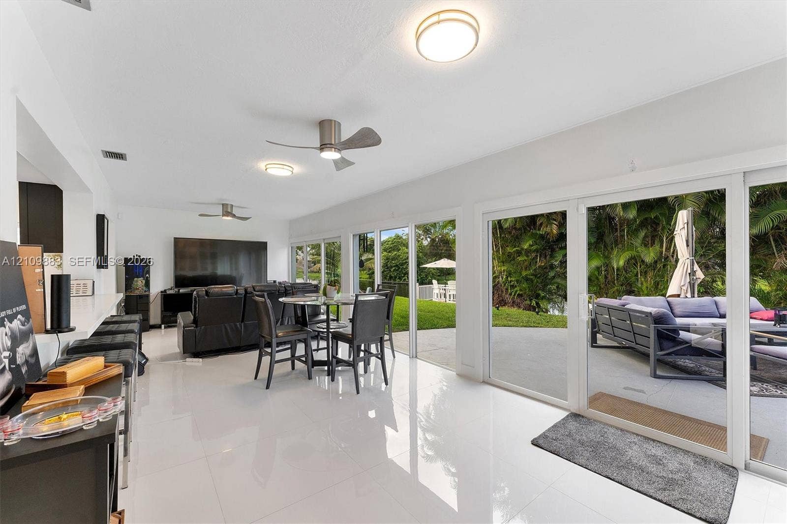 751 SW 54th Avenue, Margate, FL 33068 Open-concept living space featuring high-gloss tile flooring, three sets of floor-to-ceiling sliding glass doors, and dual brushed-nickel ceiling fans