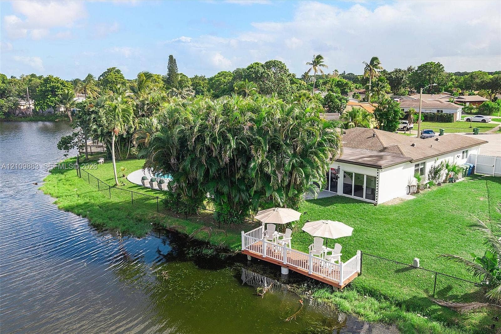 751 SW 54th Avenue, Margate, FL 33068 Waterfront property featuring a private dock with white railing, a ground-level swimming pool, expansive lawn, mature landscaping, and multi-panel sliding glass doors