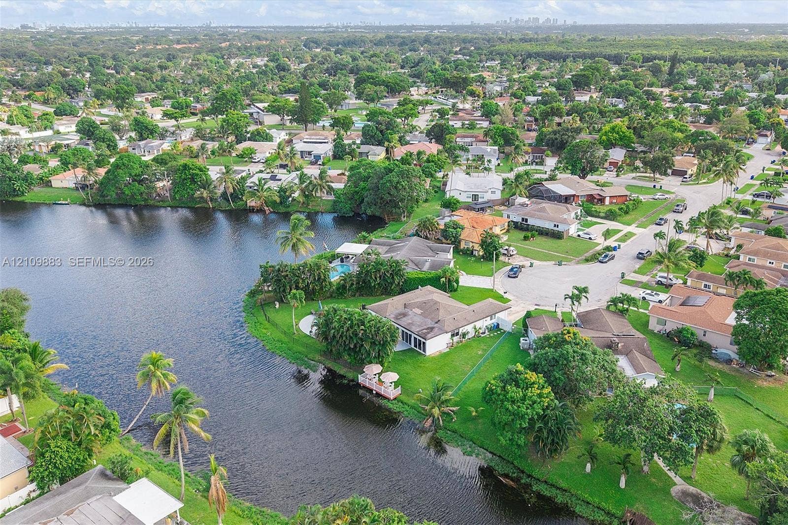 751 SW 54th Avenue, Margate, FL 33068 Waterfront property featuring a private dock, expansive lawn, mature palm trees, and an in-ground swimming pool