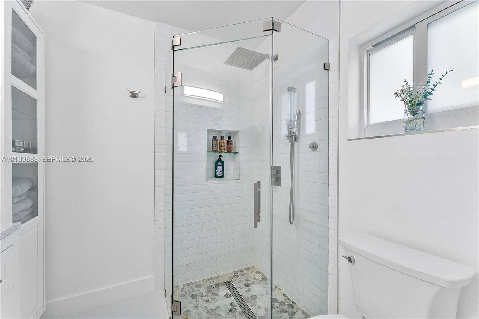 751 SW 54th Avenue, Margate, FL 33068 Walk-in glass shower with subway tile surround, integrated shelving, rainfall shower head, and stone-finish mosaic flooring