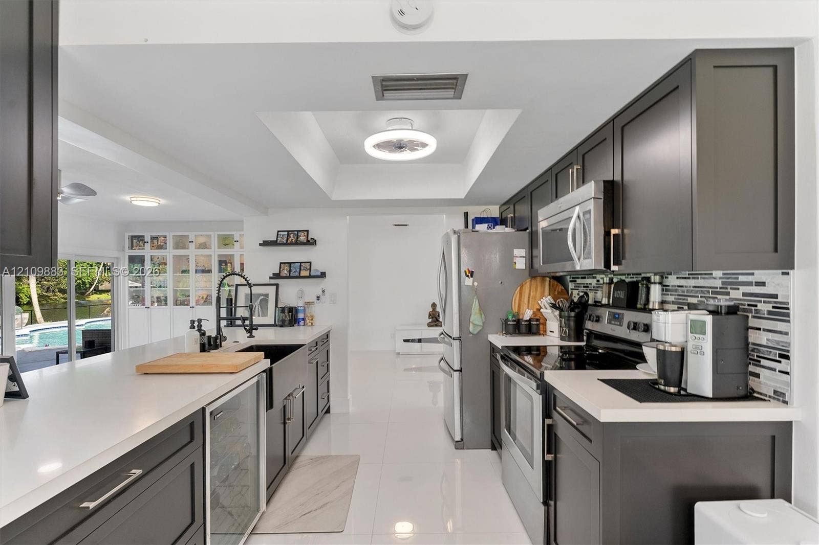 751 SW 54th Avenue, Margate, FL 33068 Kitchen featuring charcoal-toned cabinetry, quartz countertops, a farmhouse-style sink with a high-arch faucet, a built-in beverage refrigerator, and a linear mosaic tile backsplash