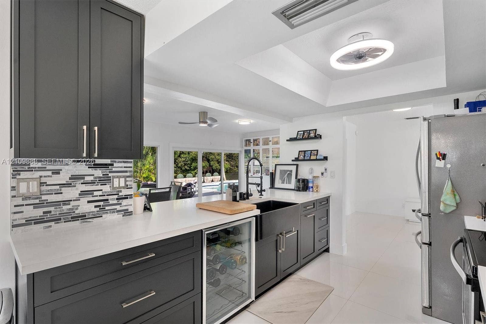 751 SW 54th Avenue, Margate, FL 33068 Kitchen featuring charcoal-toned shaker cabinetry, quartz countertops, a stone mosaic backsplash, integrated wine refrigerator, and a farmhouse-style sink with a high-arch faucet