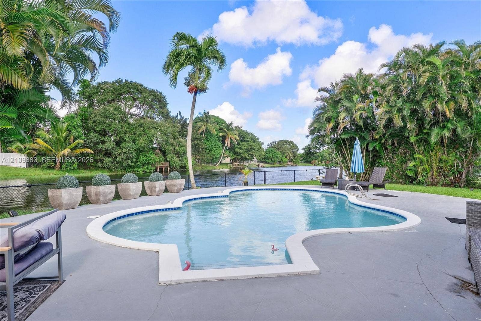 751 SW 54th Avenue, Margate, FL 33068 Custom-shaped in-ground pool with concrete surround, bordered by mature landscaping and a canal waterfront setting