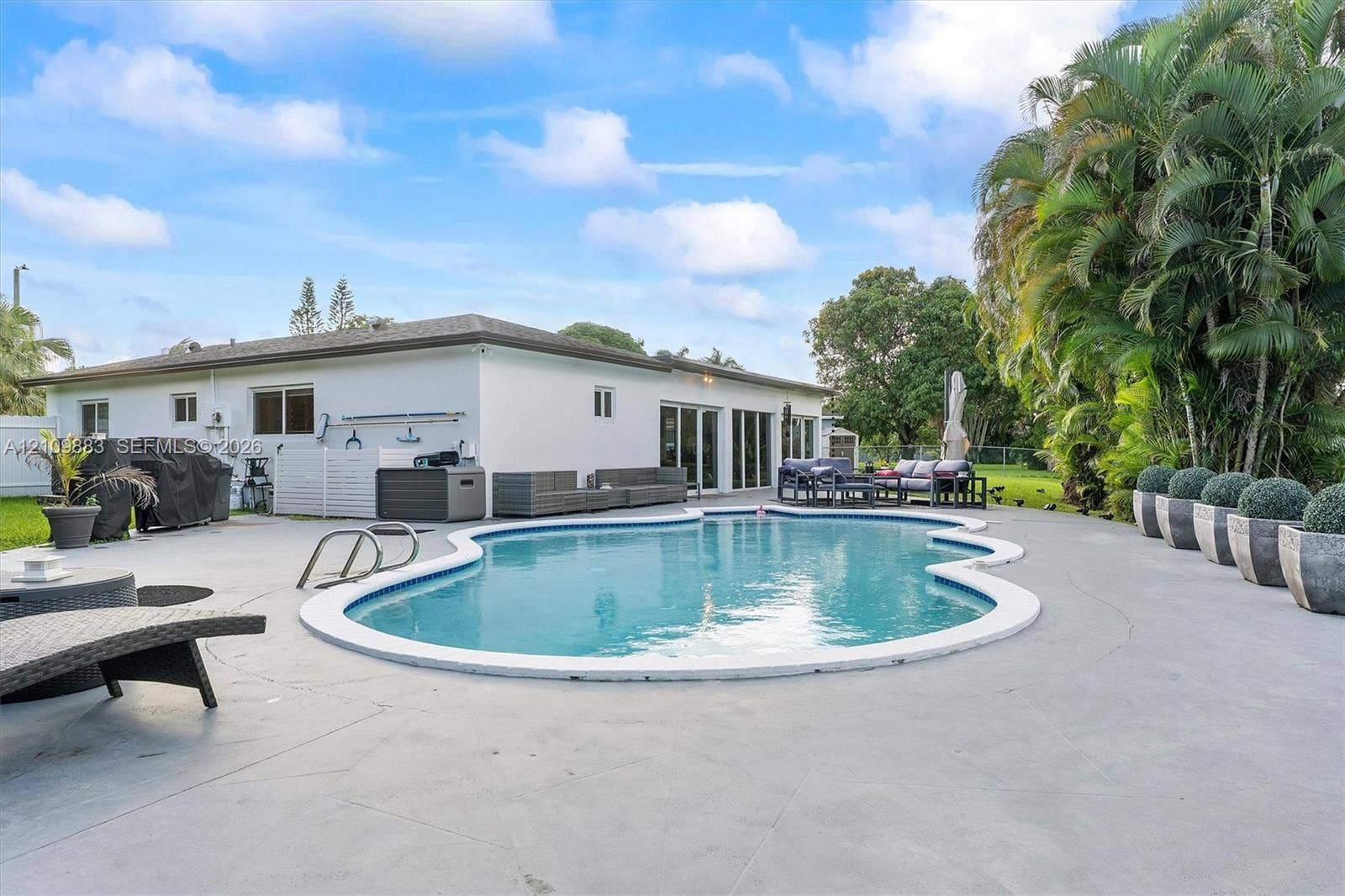 751 SW 54th Avenue, Margate, FL 33068 In-ground swimming pool with a curved perimeter, expansive concrete patio, and mature palm trees