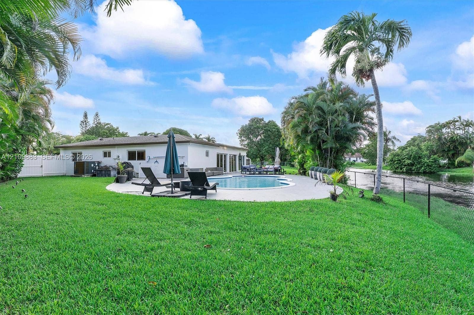 751 SW 54th Avenue, Margate, FL 33068 Backyard featuring an in-ground swimming pool, concrete patio, perimeter fencing, and mature palm trees situated along a canal