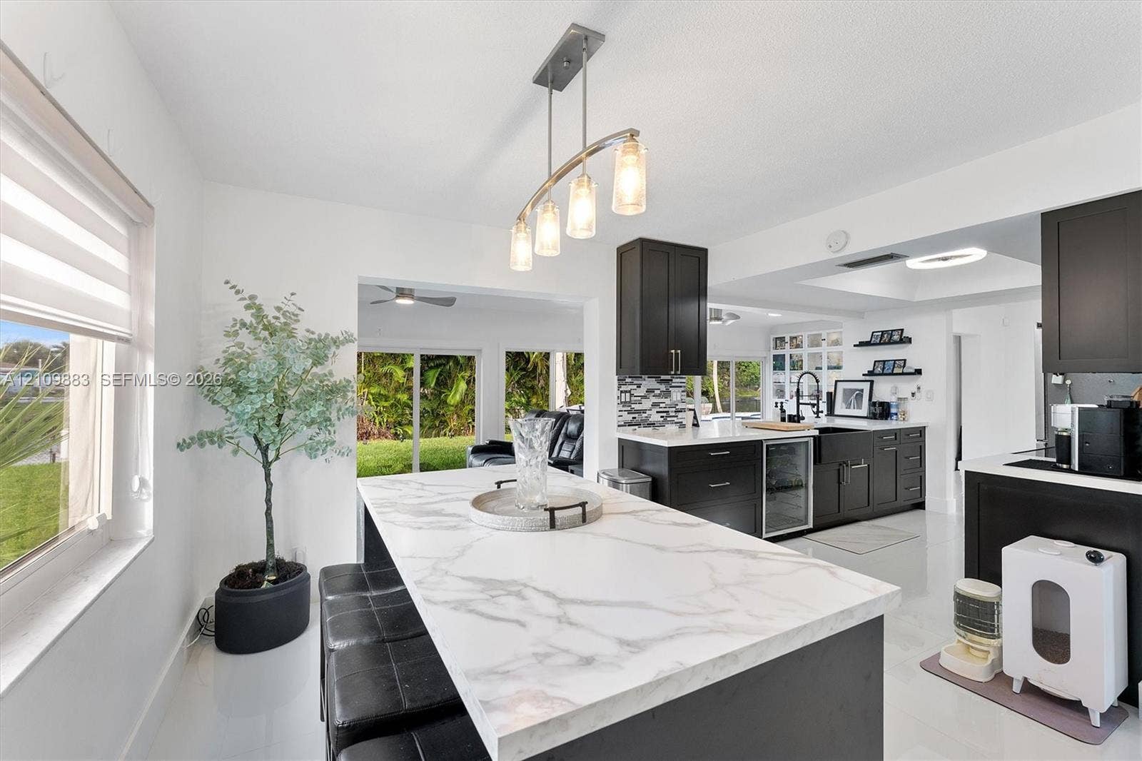 751 SW 54th Avenue, Margate, FL 33068 Kitchen featuring an expansive island with a light-toned stone-finish countertop, dark cabinetry, an integrated beverage refrigerator, a farmhouse-style sink, and a multi-light pendant fixture