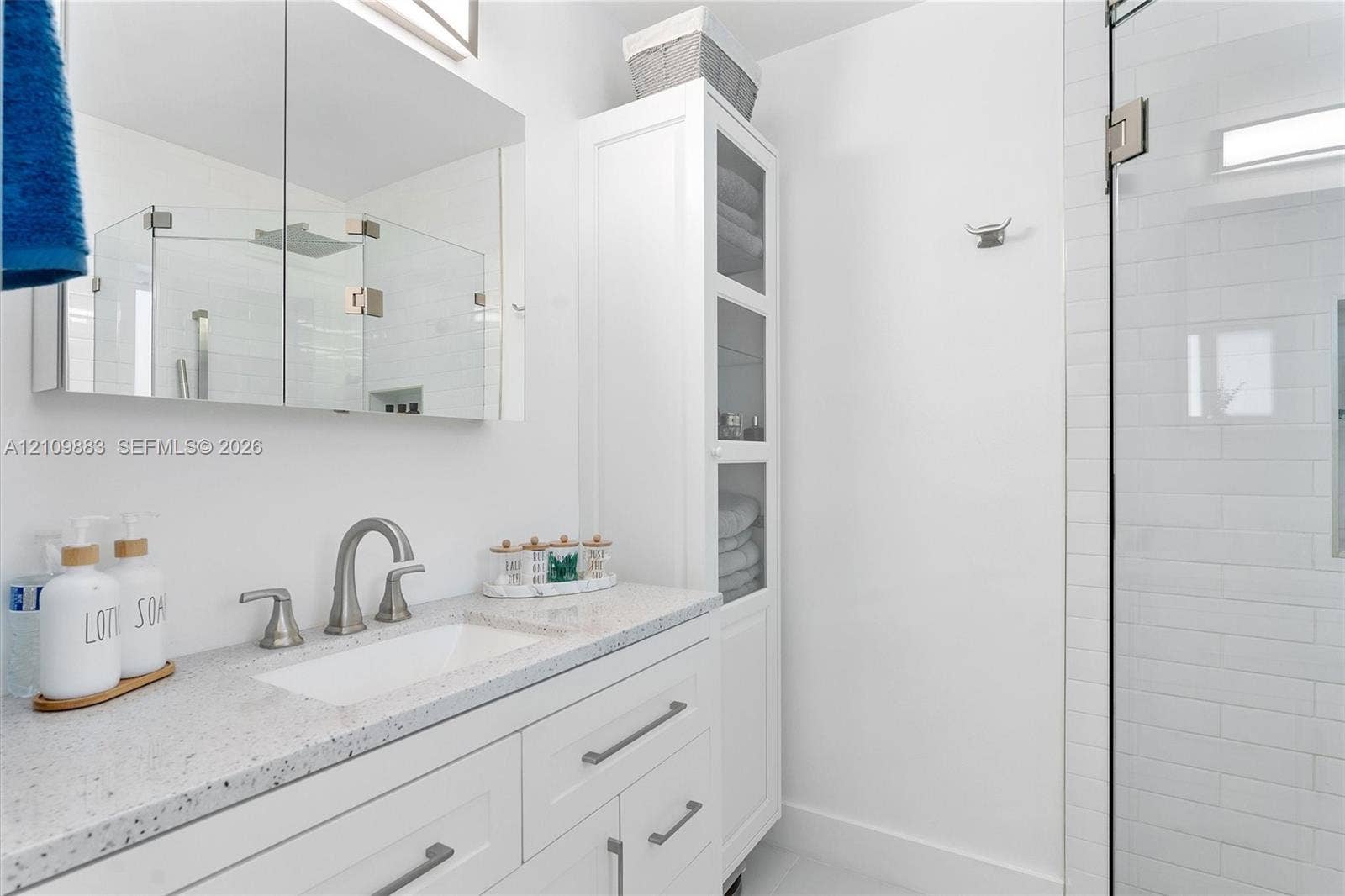 751 SW 54th Avenue, Margate, FL 33068 White vanity featuring a solid surface countertop, rectangular undermount sink, brushed nickel widespread faucet, built-in floor-to-ceiling cabinetry, and a frameless glass shower enclosure with white subway tile
