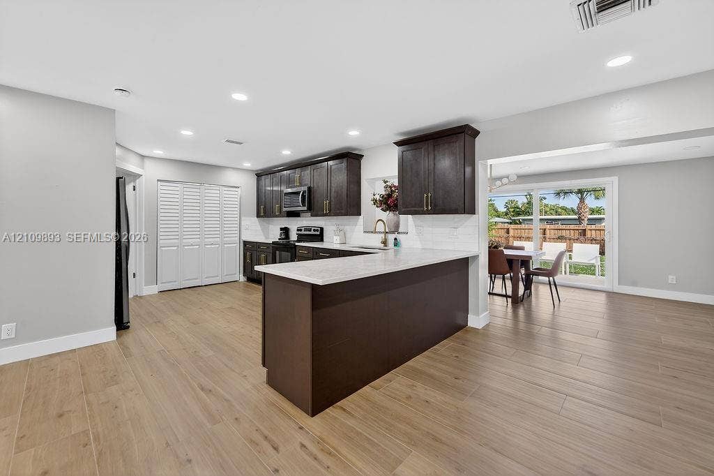 712 Tradewind Drive, North Palm Beach, North Palm Beach, FL 33408 Kitchen featuring dark wood cabinetry, quartz countertops, a breakfast bar, recessed lighting, and wood-finish flooring