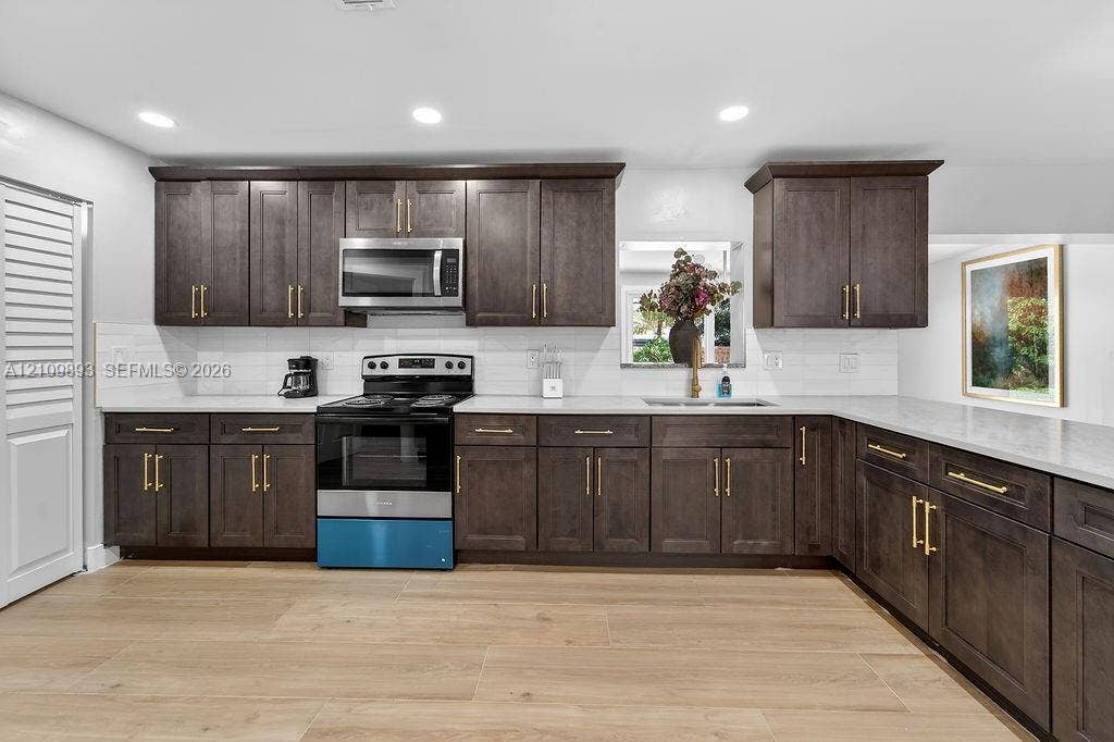 712 Tradewind Drive, North Palm Beach, North Palm Beach, FL 33408 Kitchen featuring dark-finish cabinetry with brass-tone hardware, stone countertops, white subway tile backsplash, stainless steel appliances, and wood-finish flooring