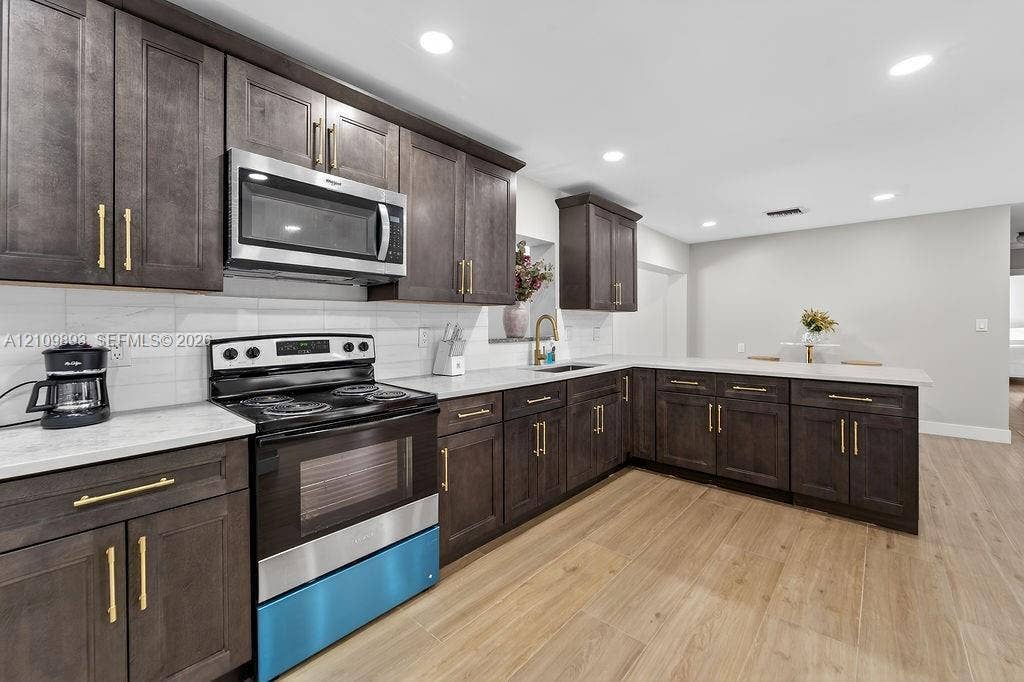712 Tradewind Drive, North Palm Beach, North Palm Beach, FL 33408 Kitchen featuring dark wood-finish cabinetry, quartz countertops, a white tile backsplash, stainless steel appliances, and wood-finish flooring