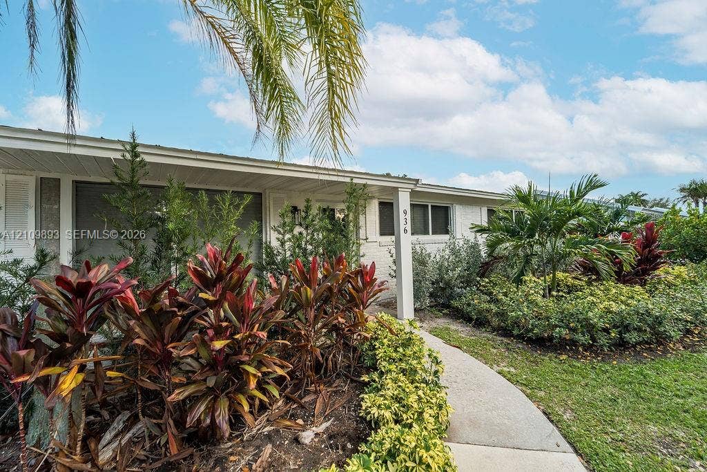 712 Tradewind Drive, North Palm Beach, North Palm Beach, FL 33408 White-painted brick exterior featuring a covered front entryway, concrete walkway, and lush tropical landscaping