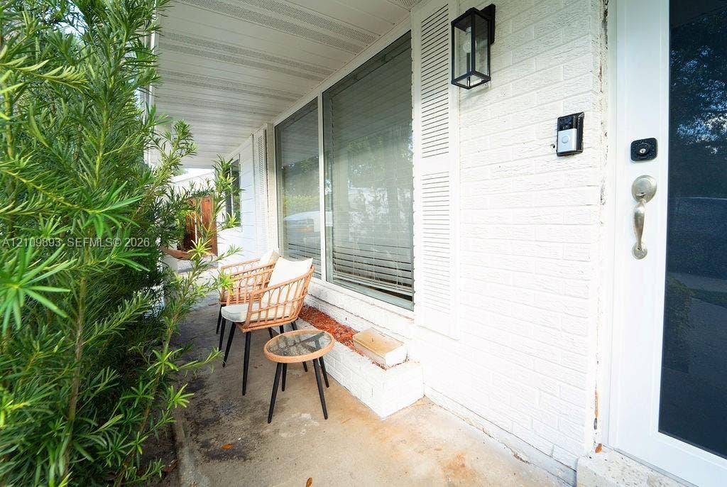 712 Tradewind Drive, North Palm Beach, North Palm Beach, FL 33408 Covered front porch featuring a painted brick exterior, built-in brick planter, decorative shutters, and an exterior wall-mounted lantern