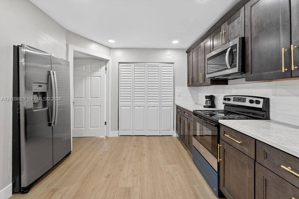712 Tradewind Drive, North Palm Beach, North Palm Beach, FL 33408 Kitchen featuring wood-finish flooring, dark-toned cabinetry with brass-finish hardware, stainless steel appliances, light-toned countertops, and a white subway tile backsplash