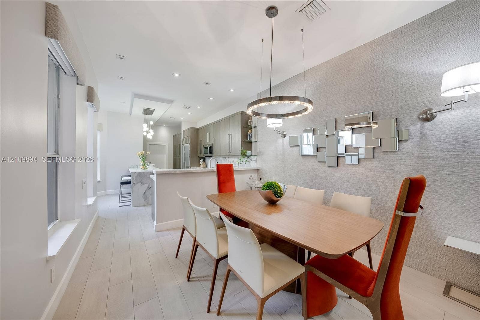 Light-toned wood-finish flooring, circular LED chandelier, textured wall covering, recessed ceiling lighting, and quartz-topped island with stone-finish waterfall edge
