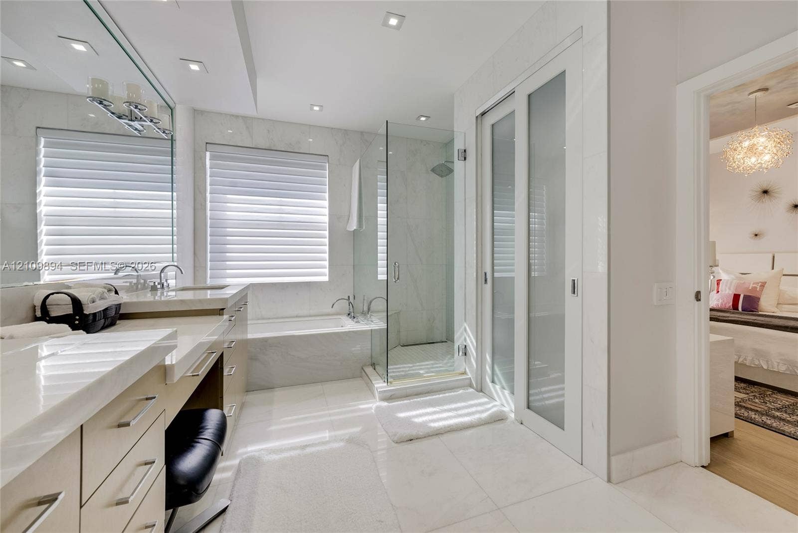 Bathroom featuring a dual-sink vanity with stone countertops, a deep soaking tub, a glass-enclosed shower, and frosted-glass sliding doors with recessed lighting