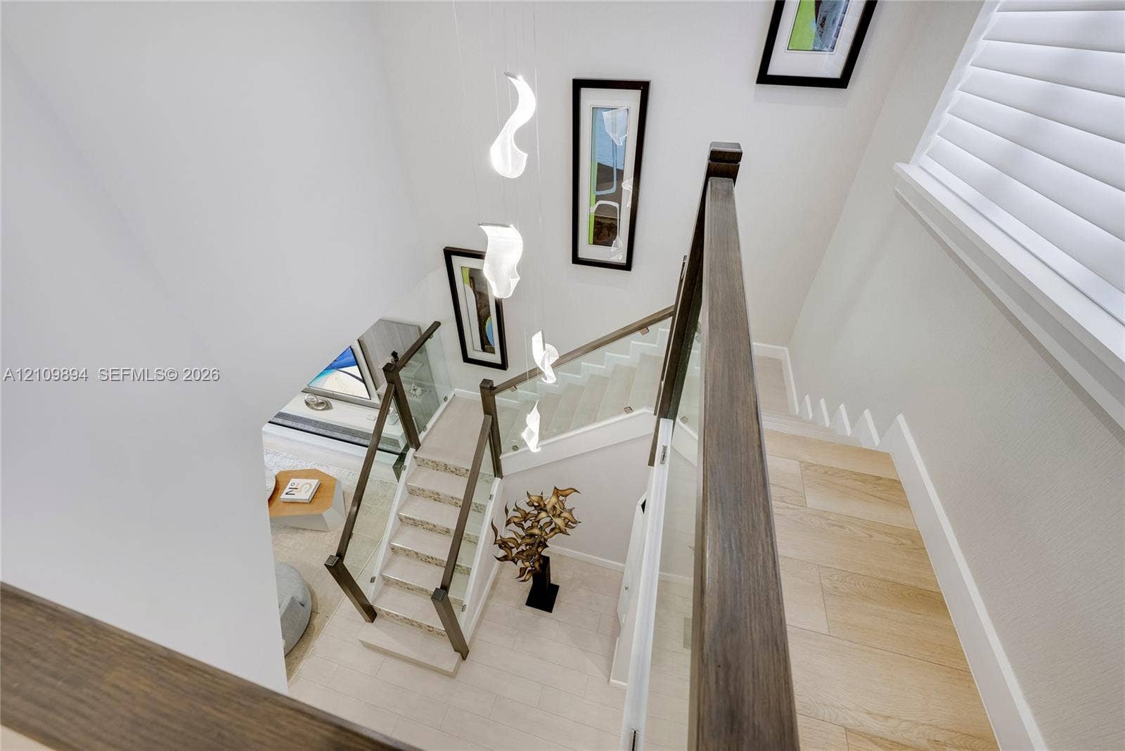 Staircase featuring glass panel railings, wood-finish handrails, multi-tiered sculptural pendant lighting, and light-toned flooring