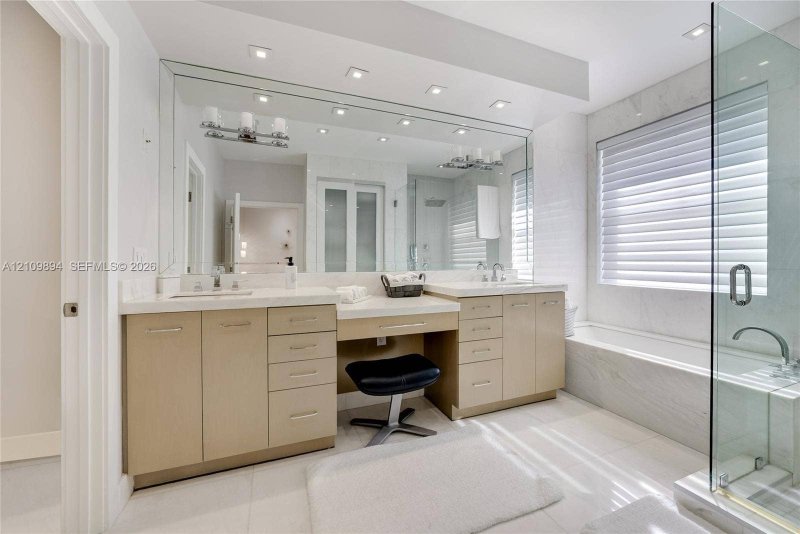 Dual vanity with integrated stone-finish countertop, recessed lighting, expansive wall-to-wall mirror, glass-enclosed shower, and a built-in soaking tub with stone-finish surround