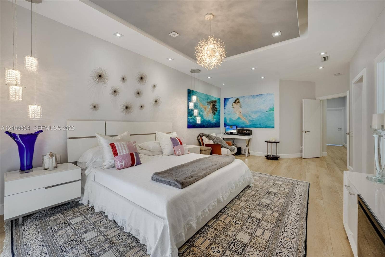 Tray ceiling featuring recessed lighting and a central decorative pendant, accompanied by wood-finish flooring and modern multi-light wall fixtures