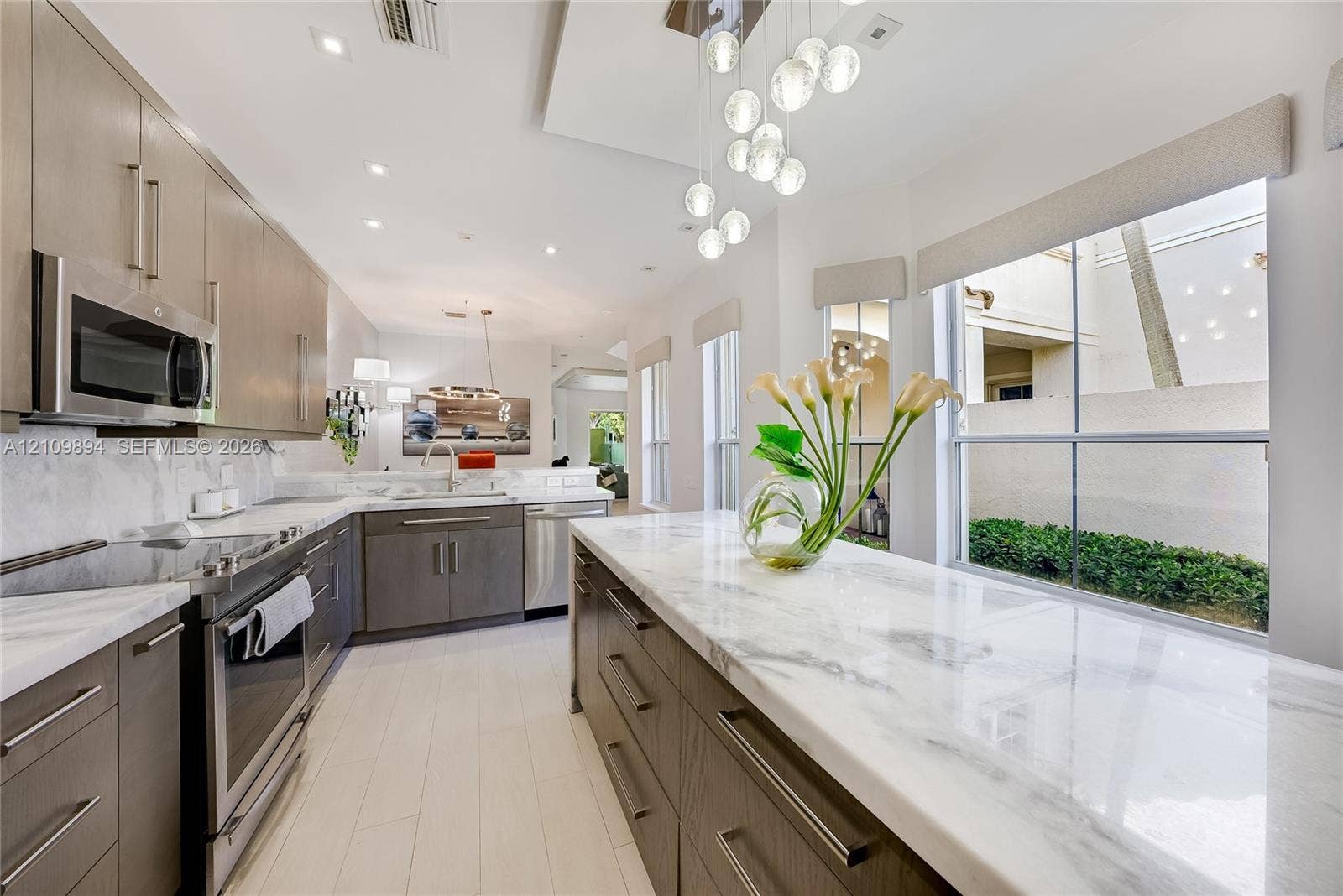 Kitchen featuring wood-finish cabinetry, stone countertops, stainless steel appliances, recessed ceiling lighting, and a multi-globe pendant light fixture