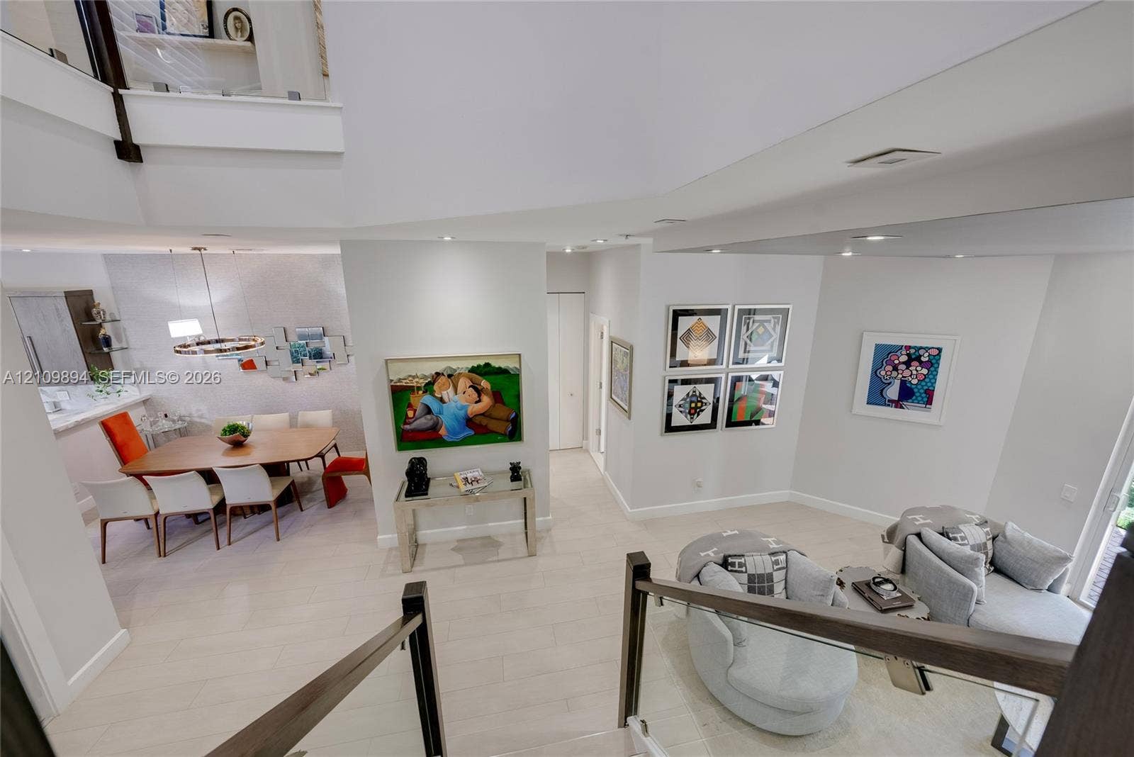 Open-concept living space featuring high ceilings, neutral-toned flooring, glass panel stair railing, and recessed lighting