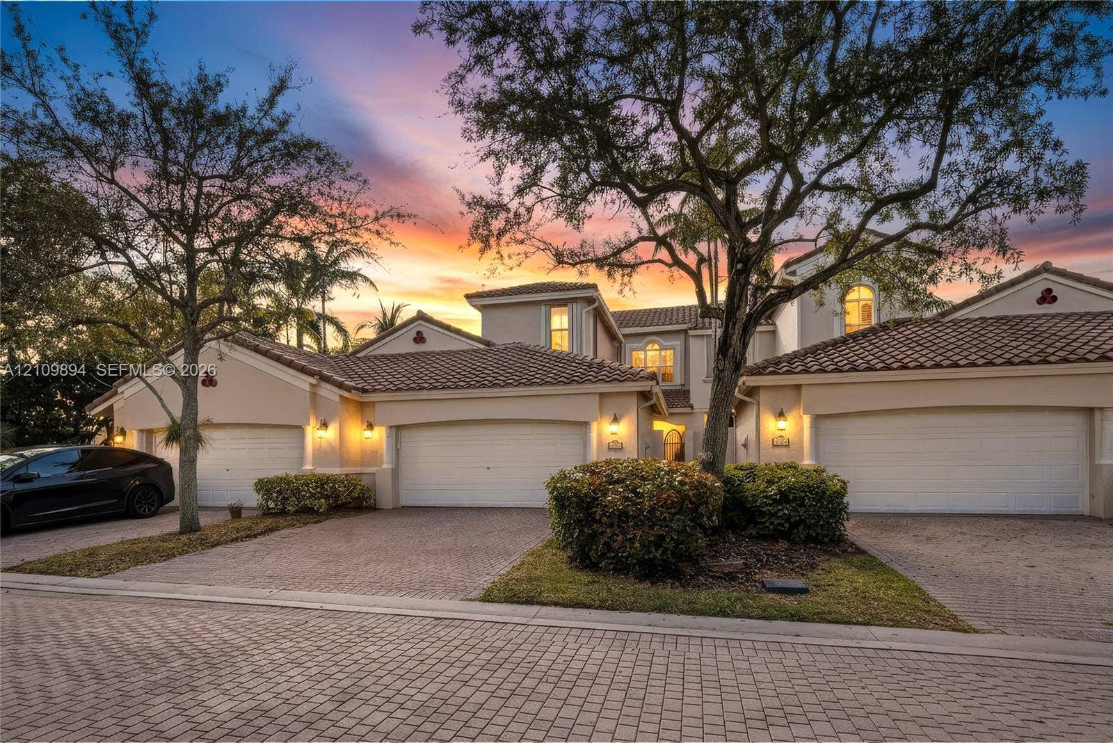 Stucco exterior residence featuring a multi-car garage, clay tile roofing, and decorative masonry paver driveway