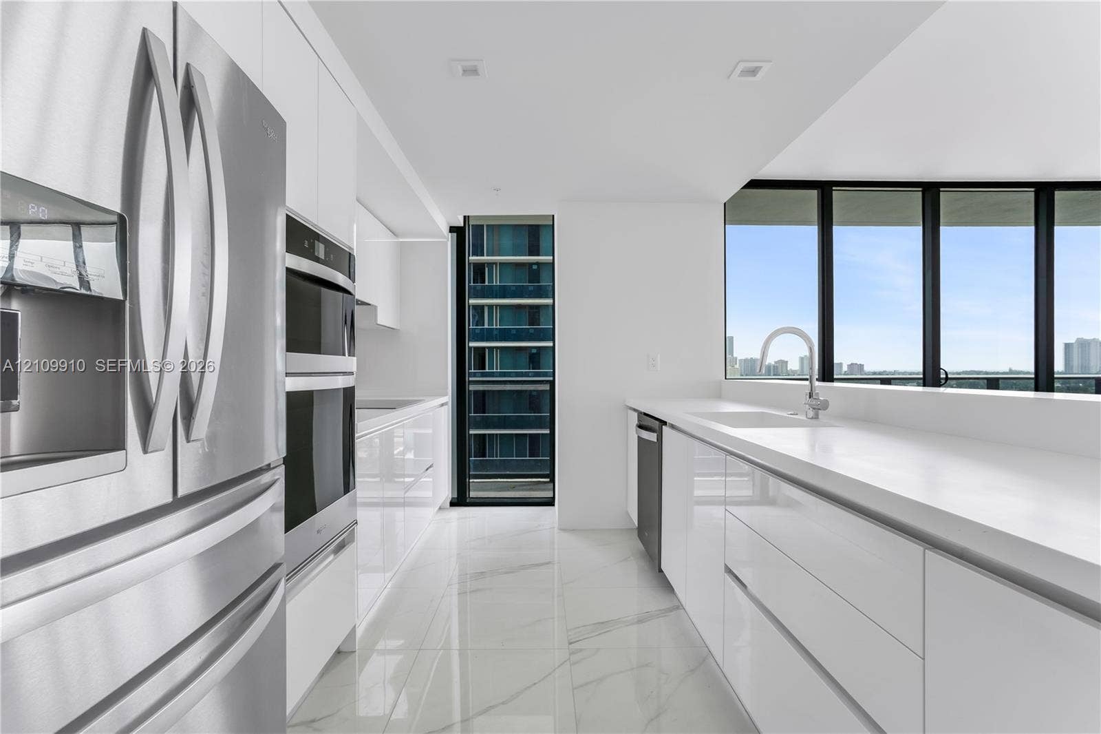 1170 E Hallandale Beach Boulevard, #908, Hallandale Beach, FL 33009 Contemporary kitchen featuring high-gloss cabinetry, stone-finish flooring, quartz countertops, stainless steel appliances, and floor-to-ceiling windows