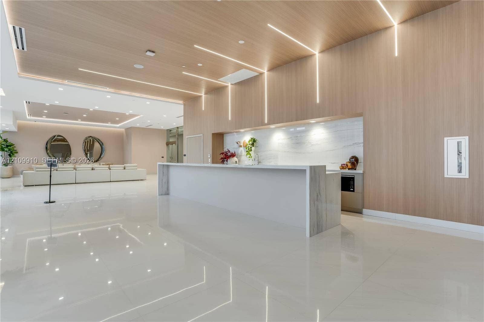 1170 E Hallandale Beach Boulevard, #908, Hallandale Beach, FL 33009 Modern lobby featuring high-gloss tile flooring, floor-to-ceiling wood-finish wall paneling, linear recessed lighting, and a stone-topped reception desk with integrated backsplash
