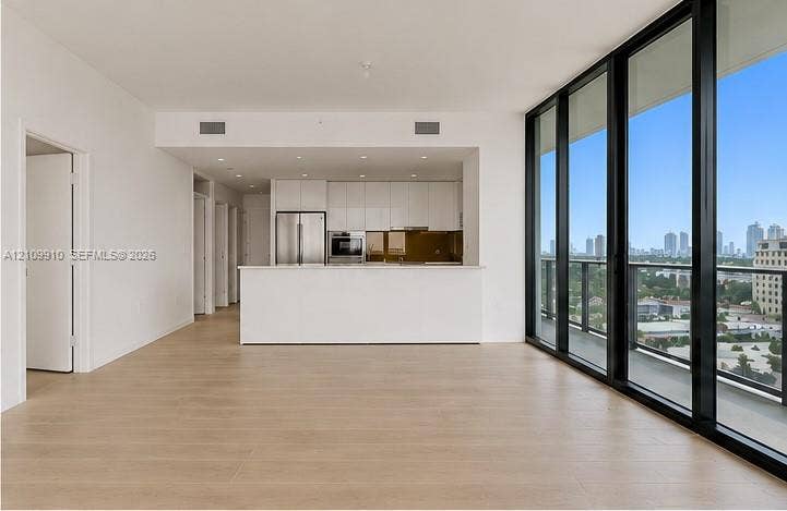 1170 E Hallandale Beach Boulevard, #908, Hallandale Beach, FL 33009 Open-concept interior featuring floor-to-ceiling glass panel walls, wood-finish flooring, white flat-panel cabinetry, stainless steel appliances, and a built-in kitchen peninsula