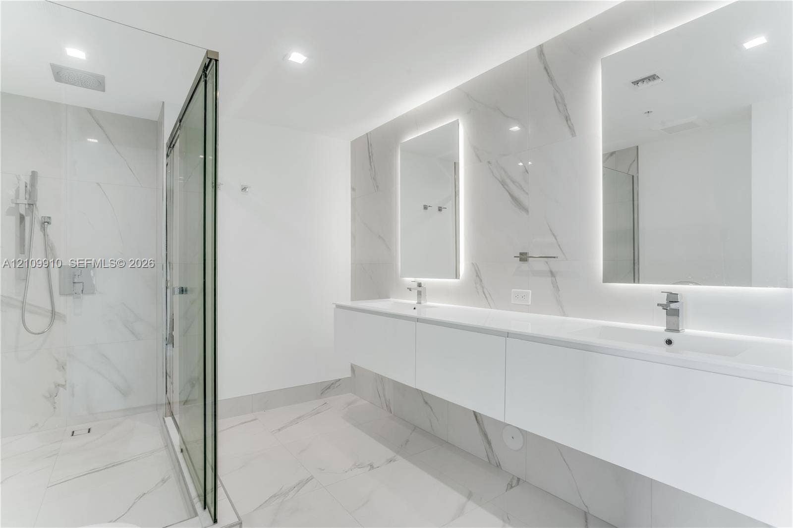 1170 E Hallandale Beach Boulevard, #908, Hallandale Beach, FL 33009 Floating double vanity with dual rectangular sinks, floor-to-ceiling stone-finish tile wall, glass-enclosed walk-in shower with rainfall fixture, and recessed LED-backlit mirrors