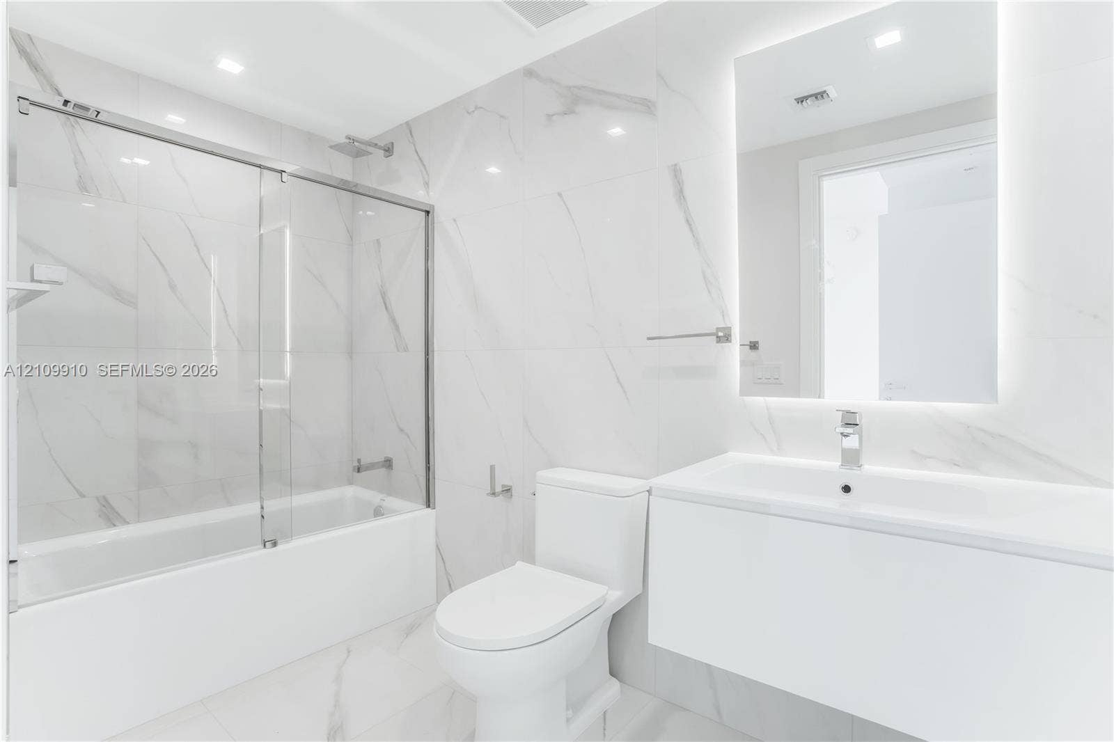 1170 E Hallandale Beach Boulevard, #908, Hallandale Beach, FL 33009 Bathroom featuring large-format porcelain tile, wall-mounted floating vanity, glass tub enclosure, and backlit vanity mirror