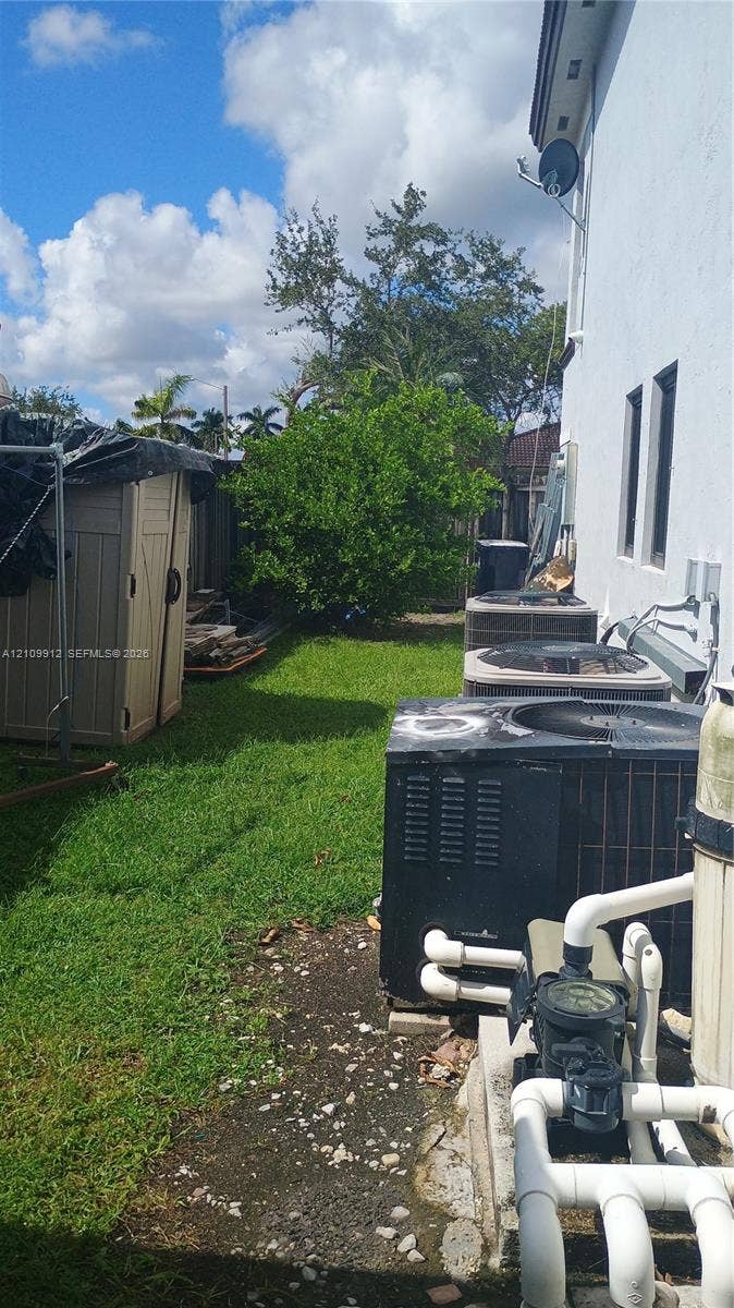 3253 SW 150 Court, Miami, FL 33185 Side yard featuring grass landscaping, mature trees, and exterior HVAC condenser units
