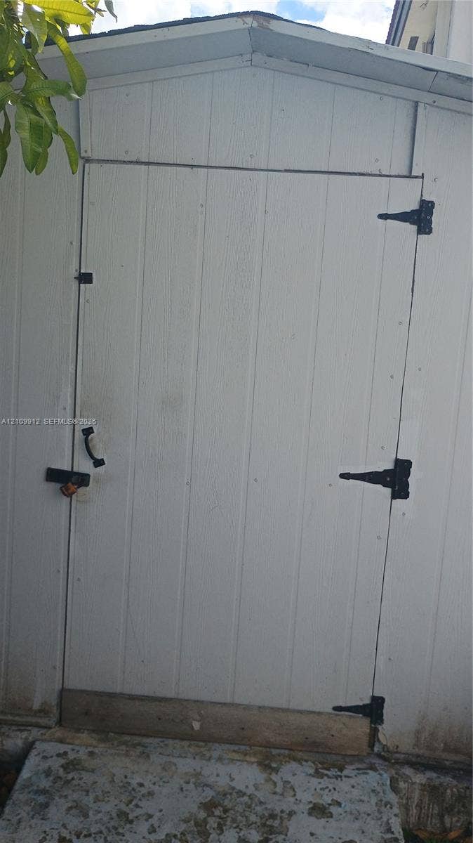 3253 SW 150 Court, Miami, FL 33185 Vertical white exterior siding, gable roofline, and black metal door hardware including hinges and a handle