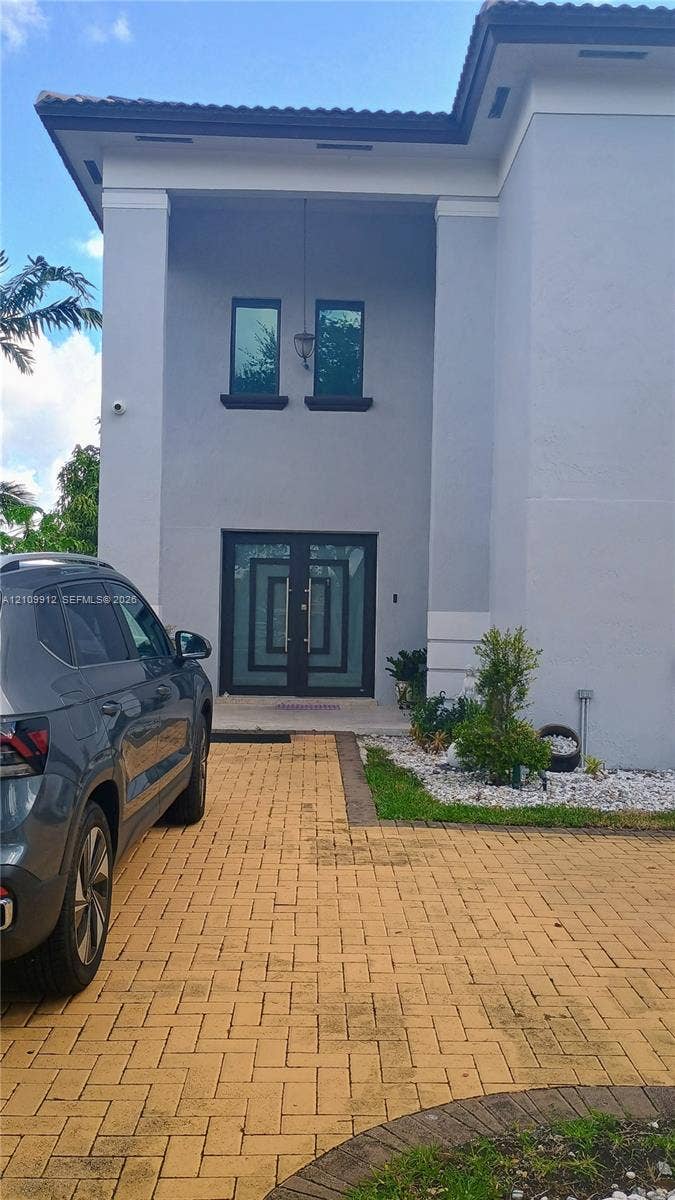 3253 SW 150 Court, Miami, FL 33185 Two-story exterior featuring a light gray facade, paver driveway, double front entry doors with geometric glass inlays, and custom exterior lighting