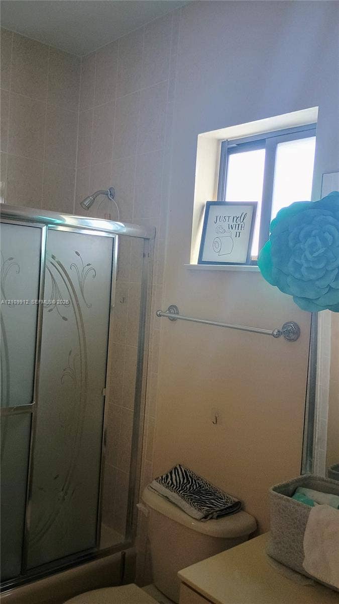 3253 SW 150 Court, Miami, FL 33185 Shower enclosure featuring sliding glass doors with etched floral patterns and tile wall surround, complemented by a horizontal metal towel bar and a recessed window