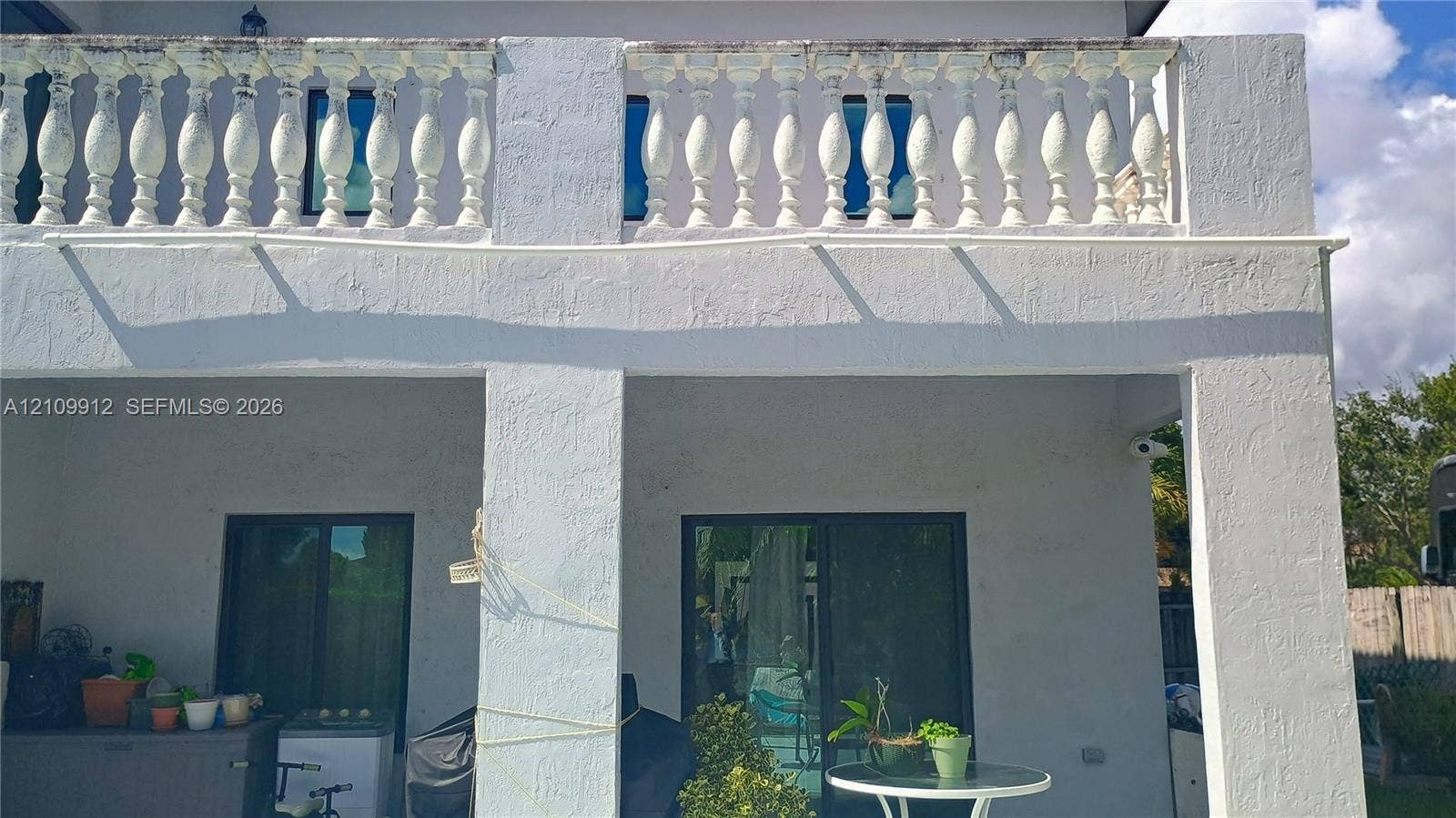 3253 SW 150 Court, Miami, FL 33185 Stucco exterior featuring a covered patio, a second-story balcony with decorative balustrade, and dual glass sliding doors