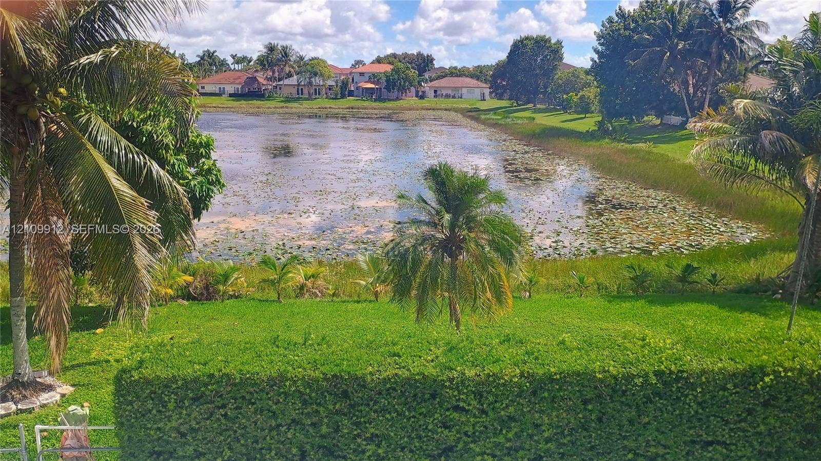 3253 SW 150 Court, Miami, FL 33185 Waterfront lot featuring a manicured lawn, mature palm trees, and native vegetation