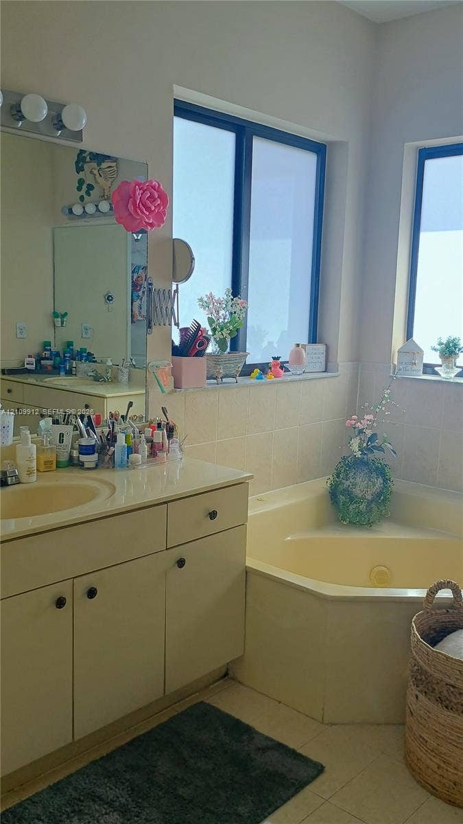 3253 SW 150 Court, Miami, FL 33185 Bathroom featuring a corner soaking tub, solid-surface vanity countertop with integrated sink, wooden cabinetry, and dual windows