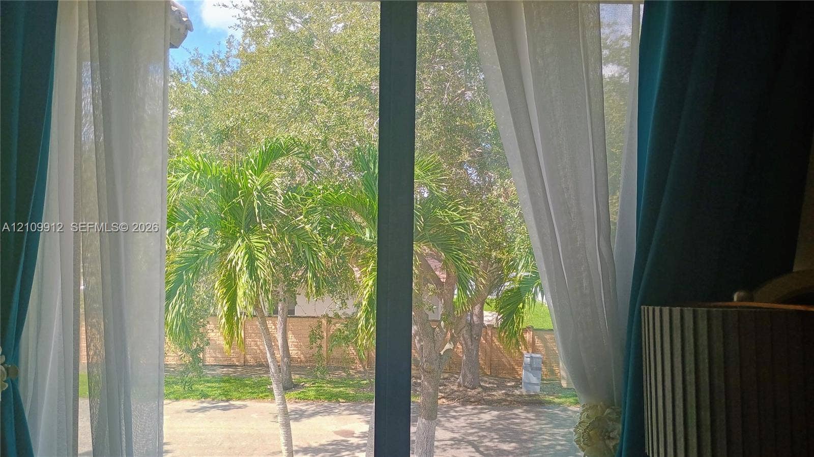 3253 SW 150 Court, Miami, FL 33185 Large glass sliding door framed by a solid vertical mullion, opening toward a fenced backyard with mature palm trees and established landscaping